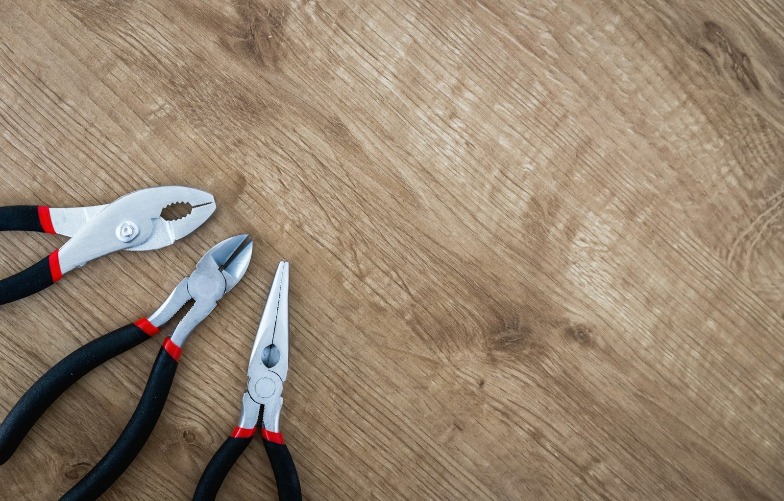 three black handled pliers on brown surface