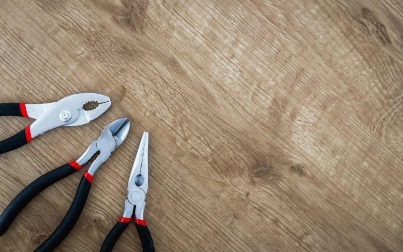 three black handled pliers on brown surface