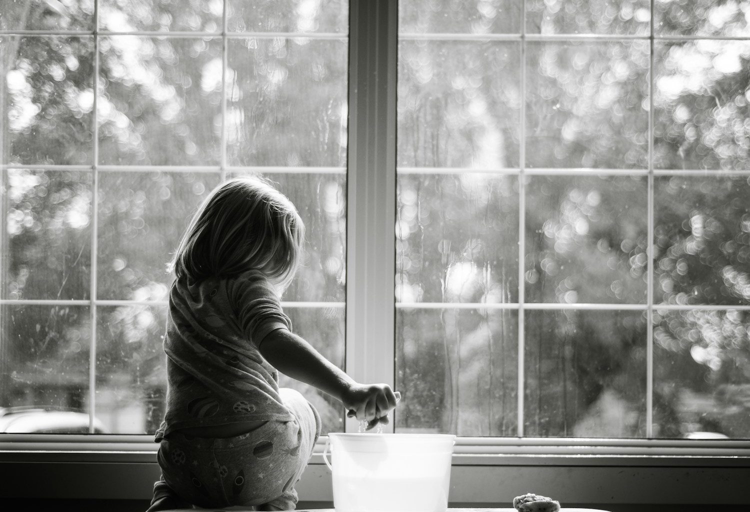 grayscale photo of woman sitting on table looking at the window
