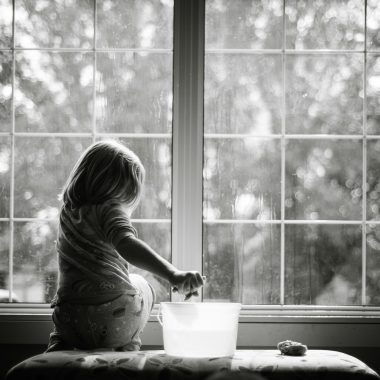 grayscale photo of woman sitting on table looking at the window