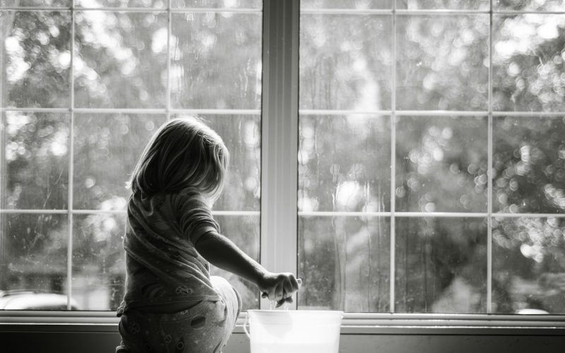 grayscale photo of woman sitting on table looking at the window