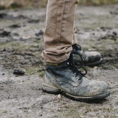 person in black work shoes standing on dirt pathway